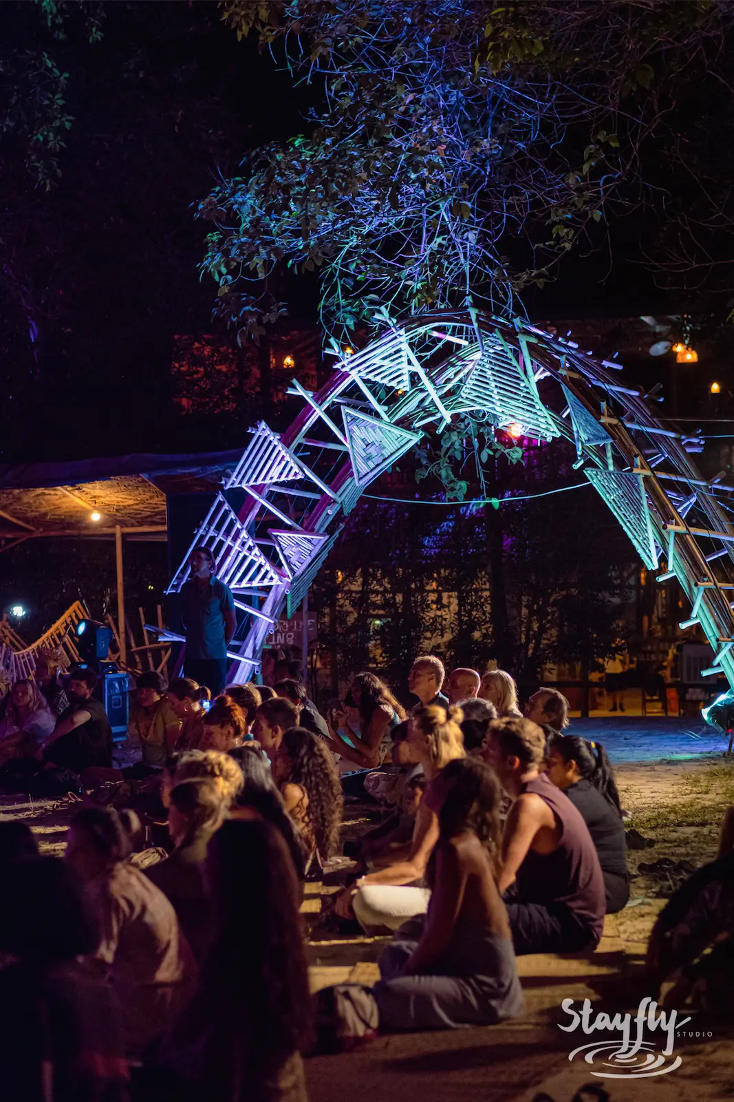 Crowd gathers beneath a lit night art installation.