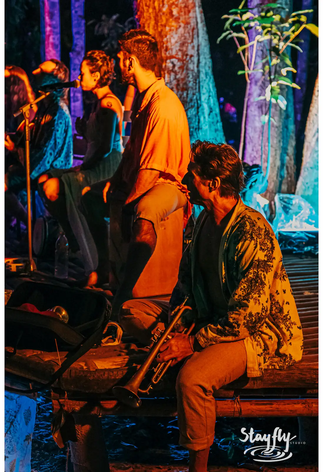 Group seated on a dock at night, colorful lights.