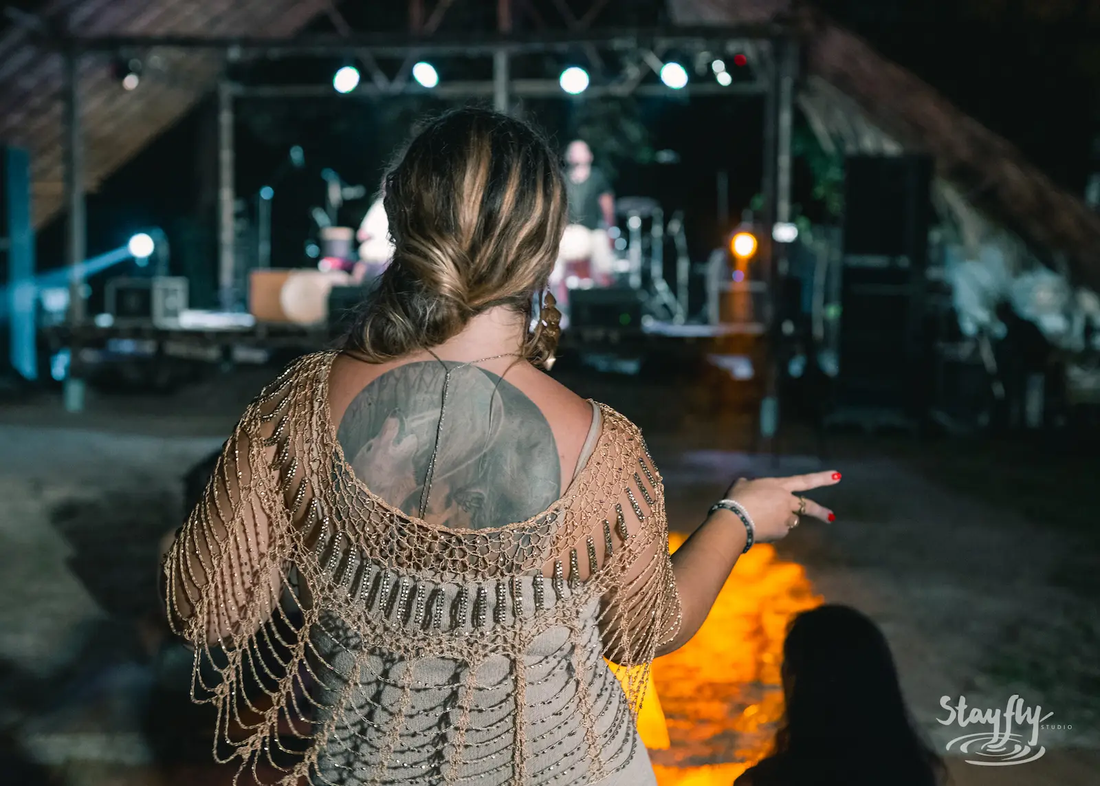 Woman viewed from behind pointing toward stage fire.