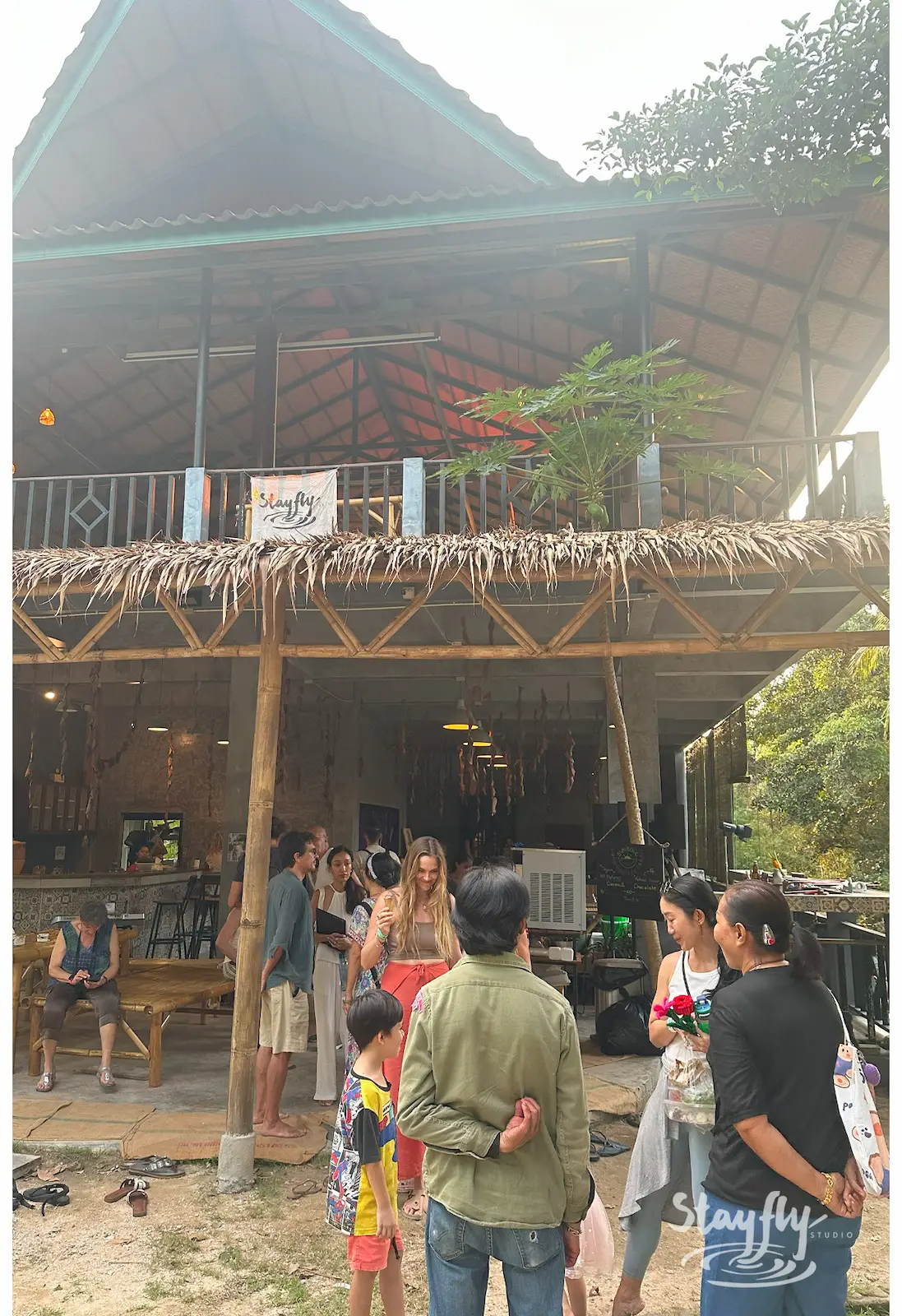 Crowd gathering outside two-story thatched venue.
