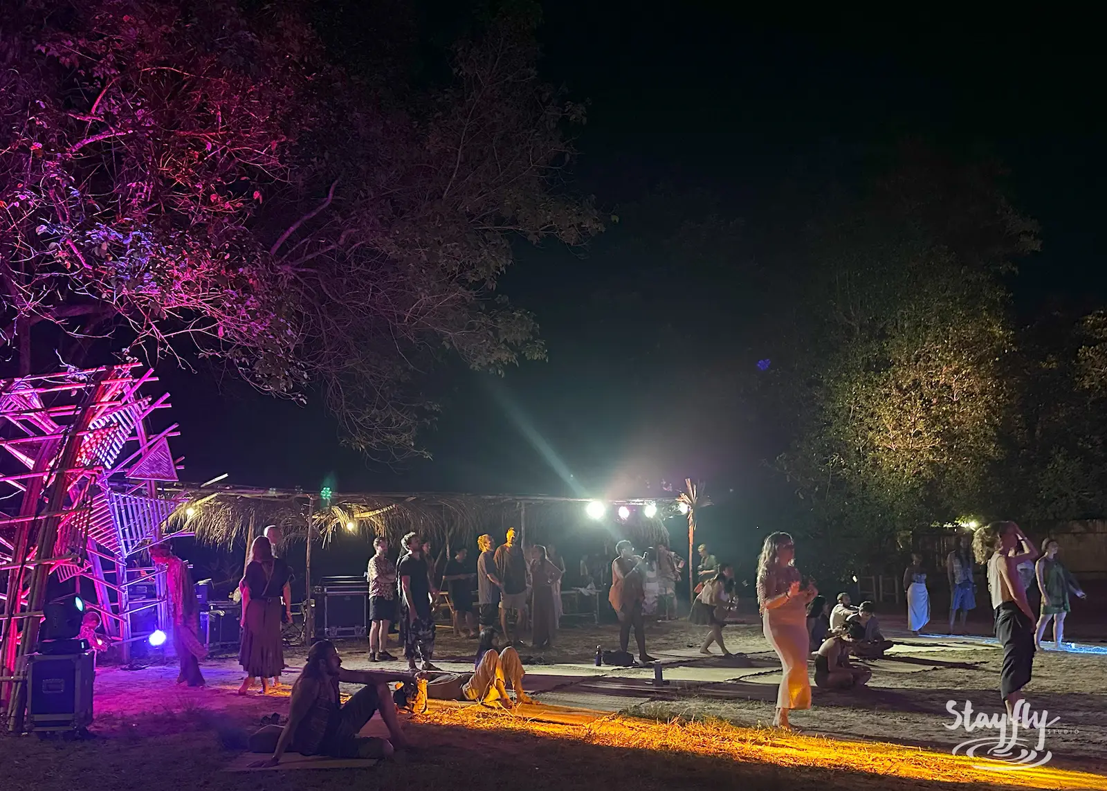 People dance near lit yellow bamboo archway.