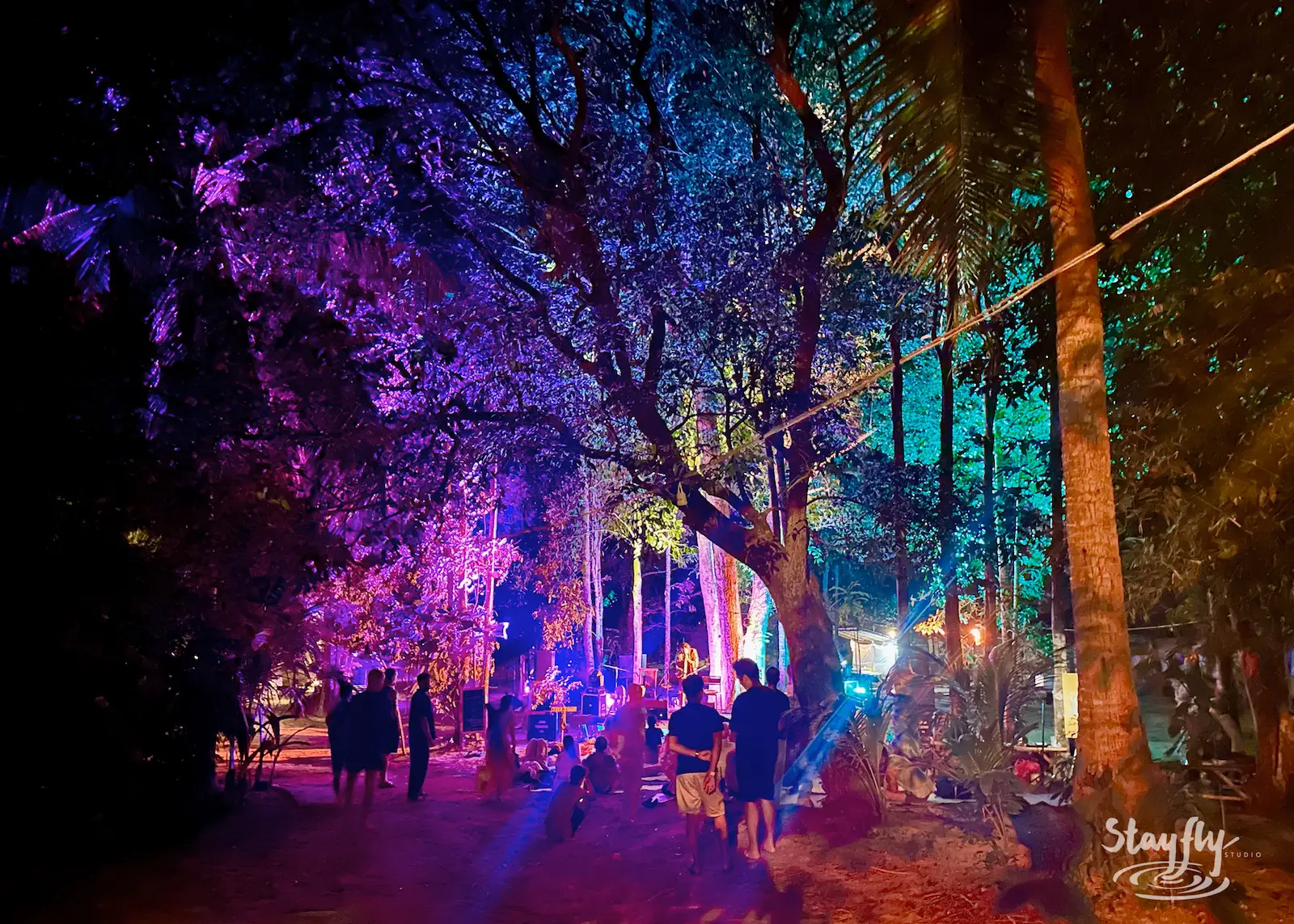 Purple-lit forest path with walking crowd.