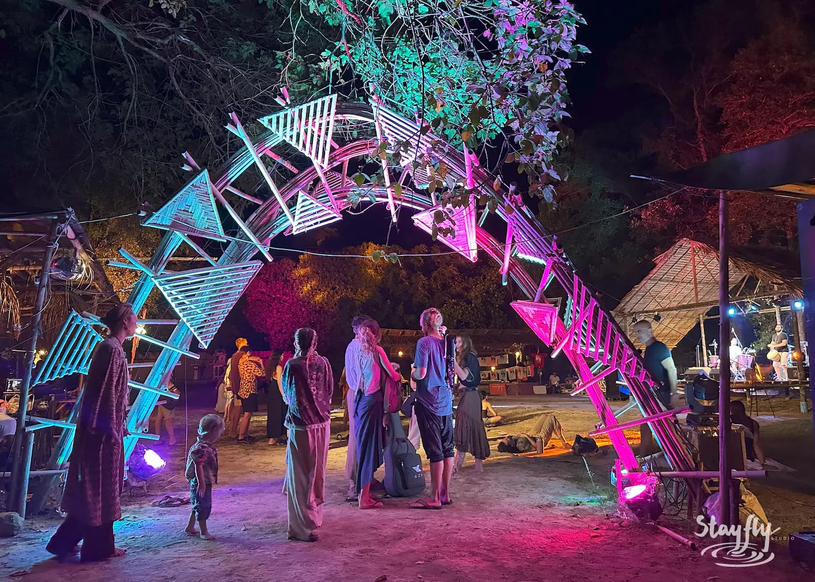 People gather under lit triangular art arch.