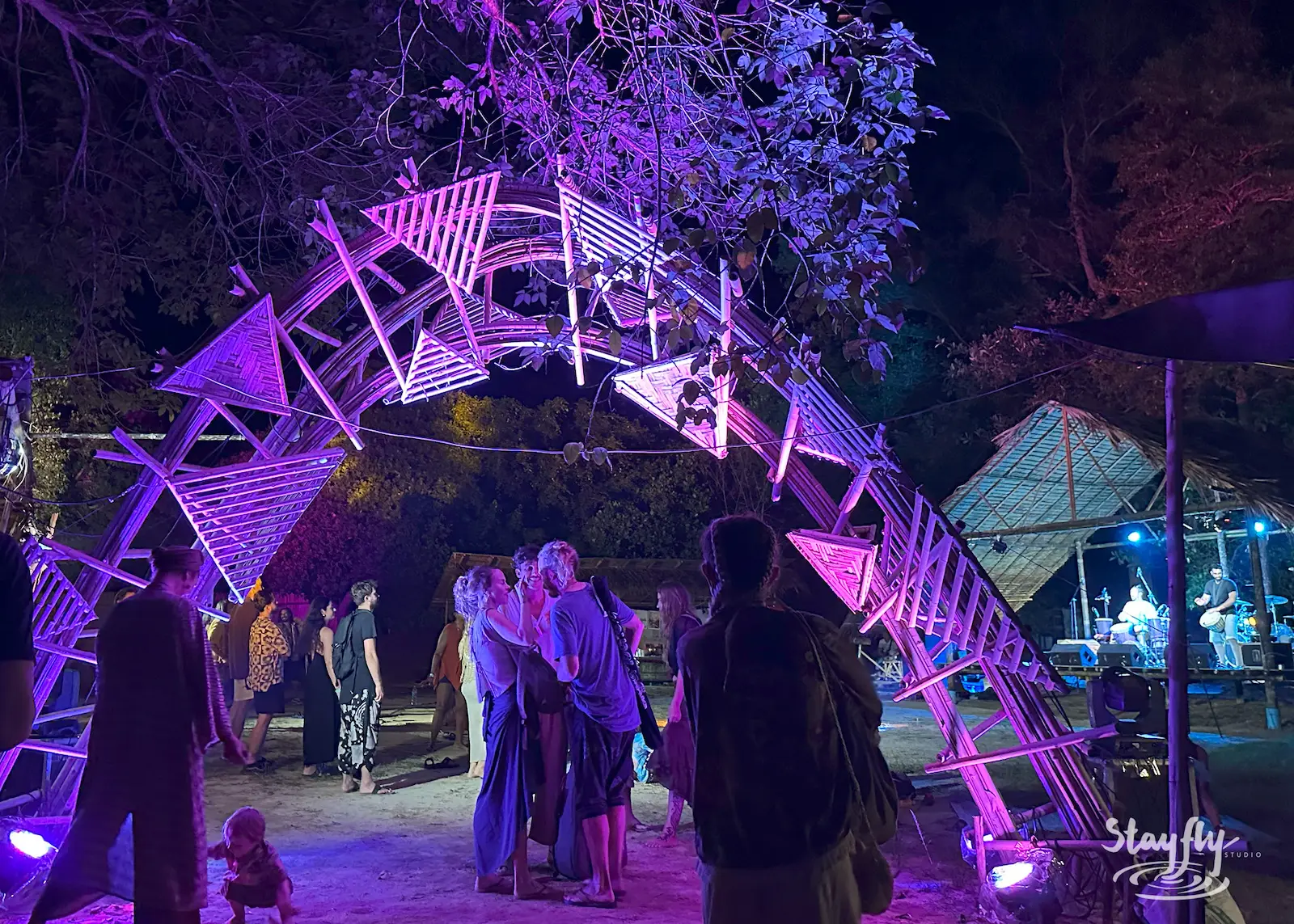 People stand near pink-lit arch at night.