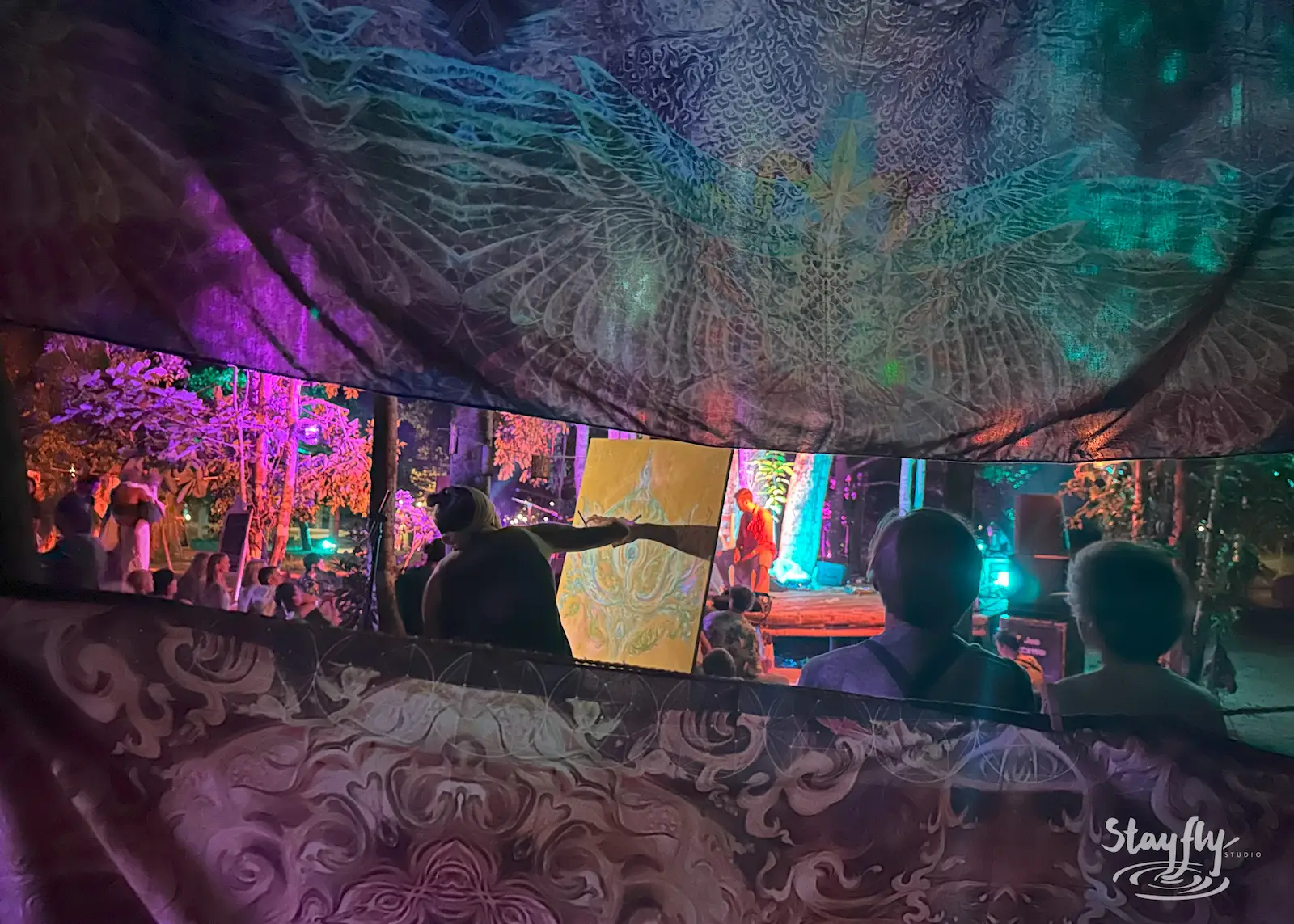 People inside art-draped tent view bright screen.