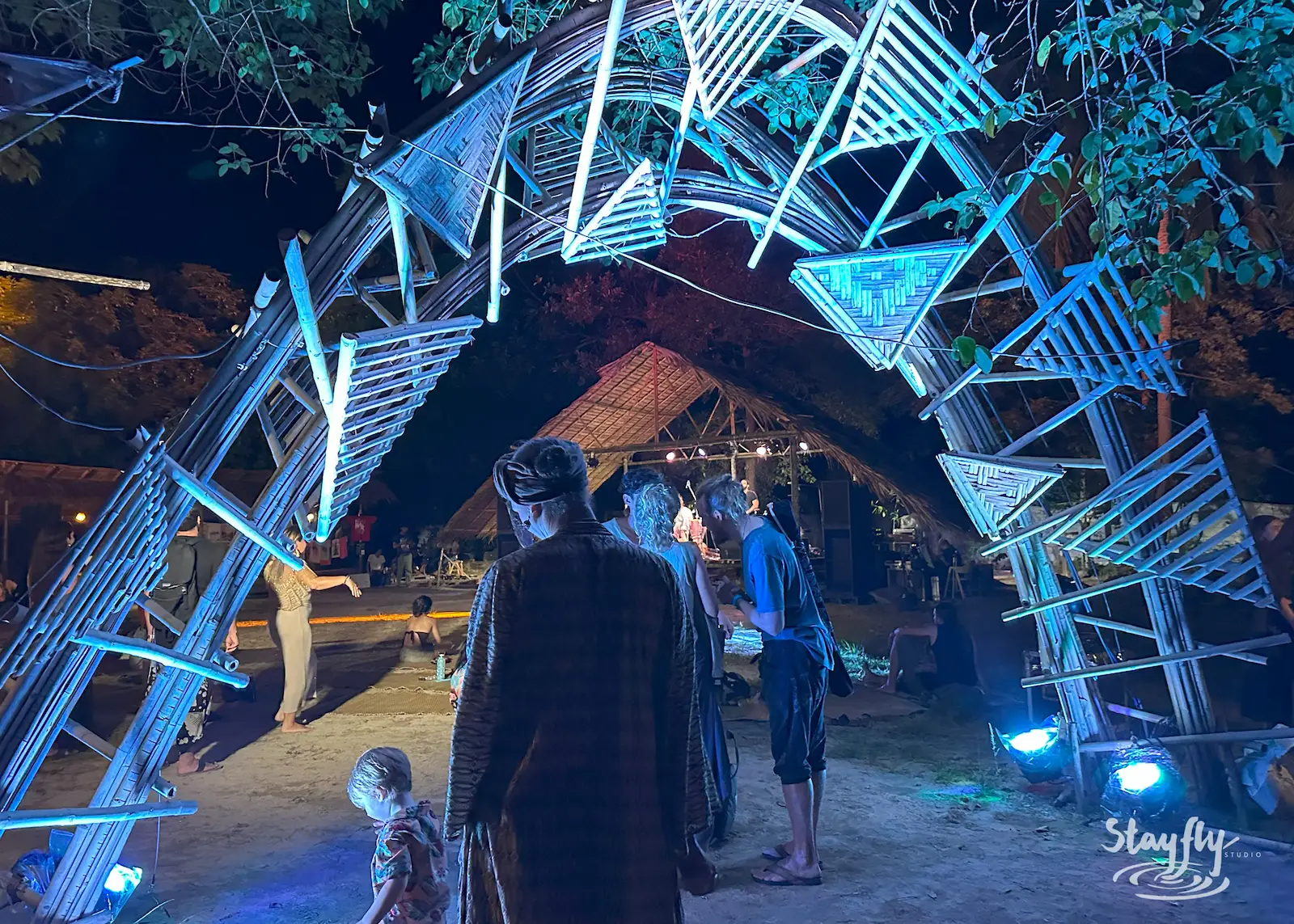 People walk through lit geometric arch at night.