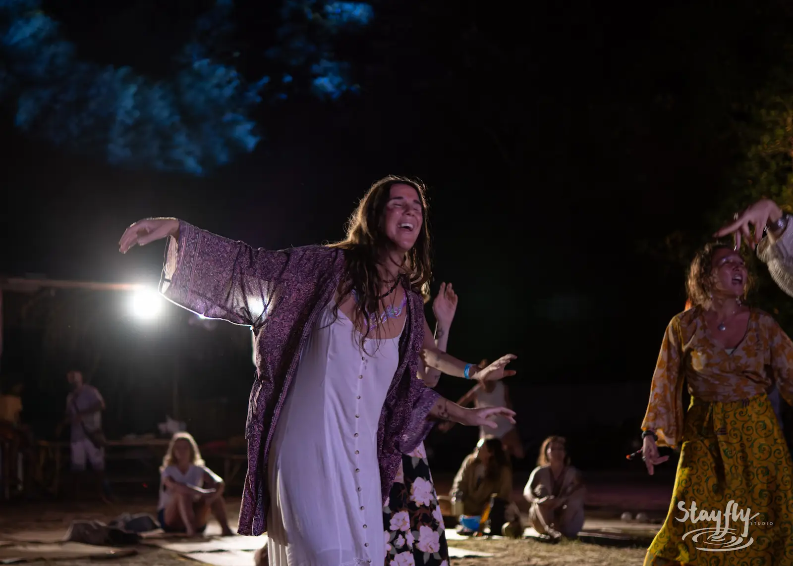 Woman dances with arms raised at night.