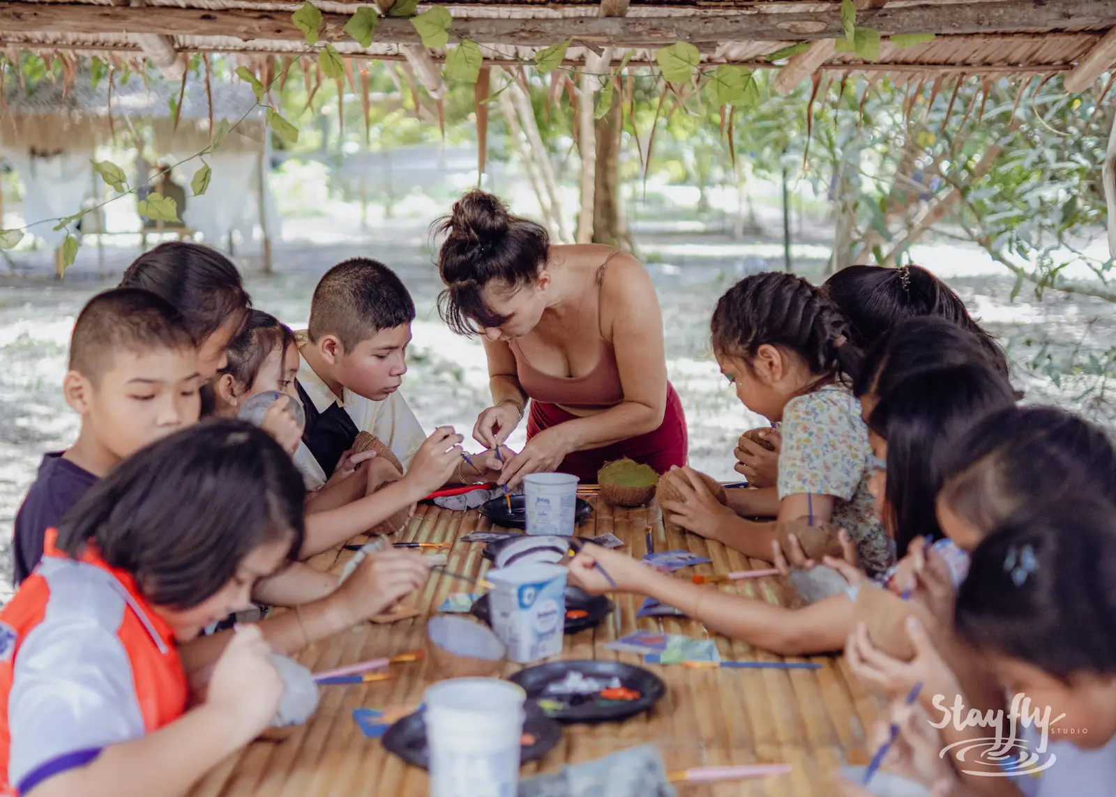Children paint crafts at outdoor table.