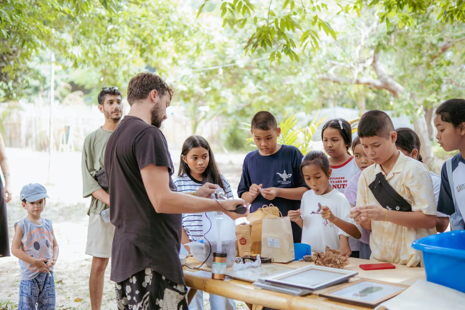 Children gather at table receiving craft materials outdoors.