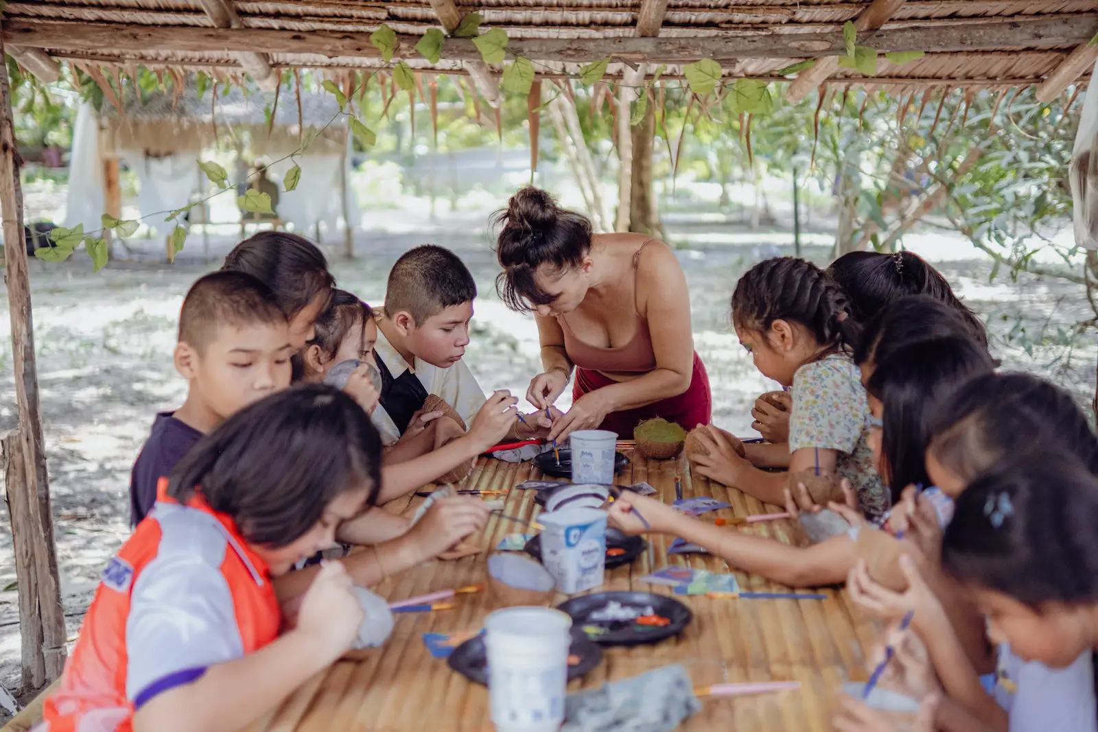 Children and helper do craft activity at table.
