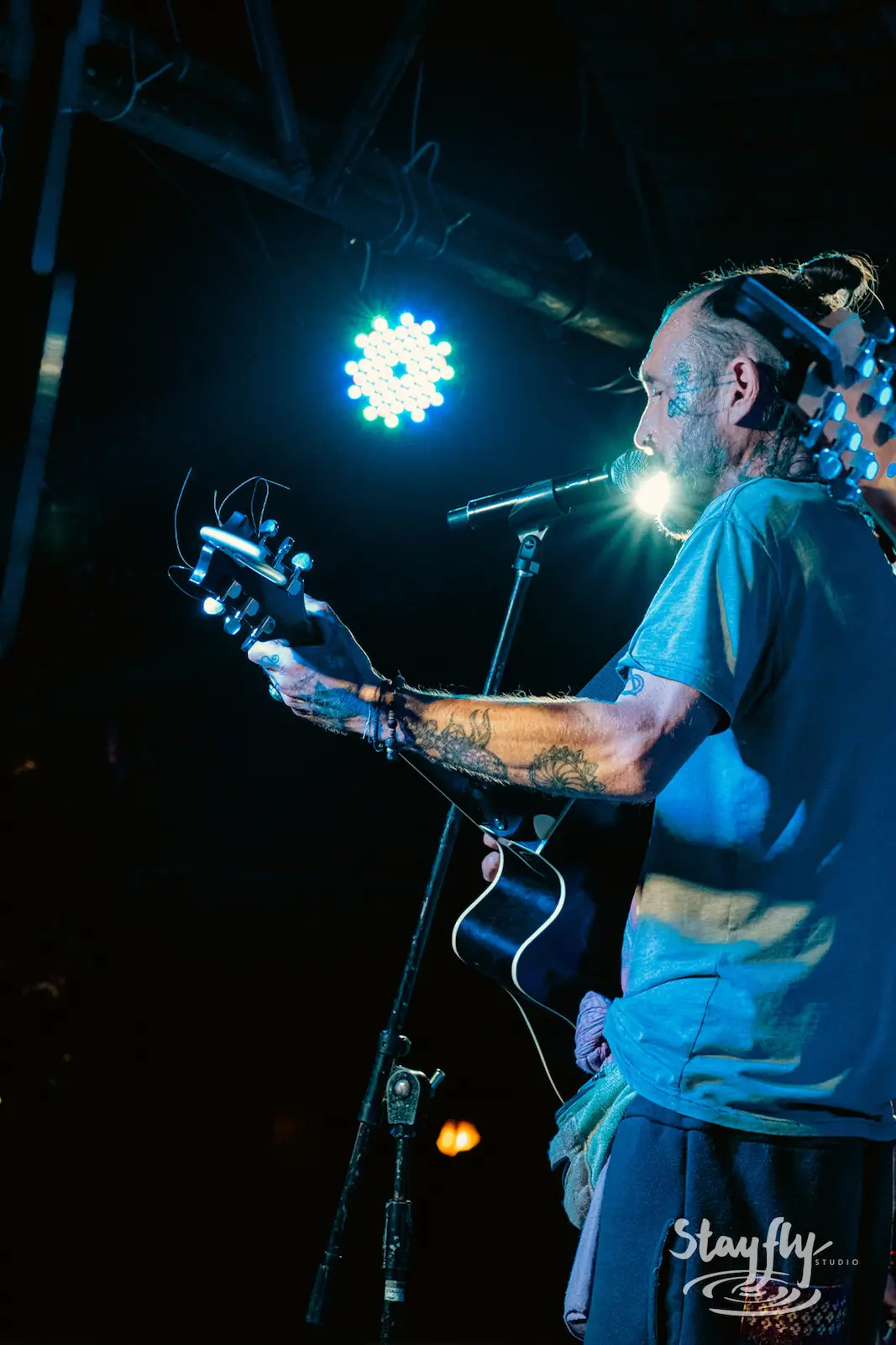 Bearded guitarist singing under colorful stage lights.