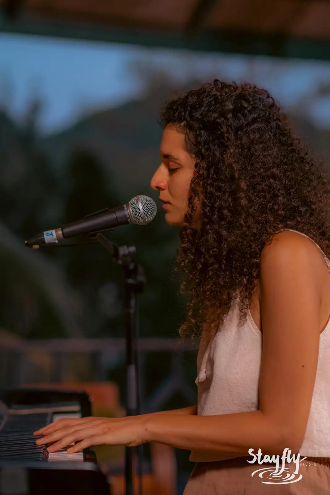 Woman sings at piano during golden hour.