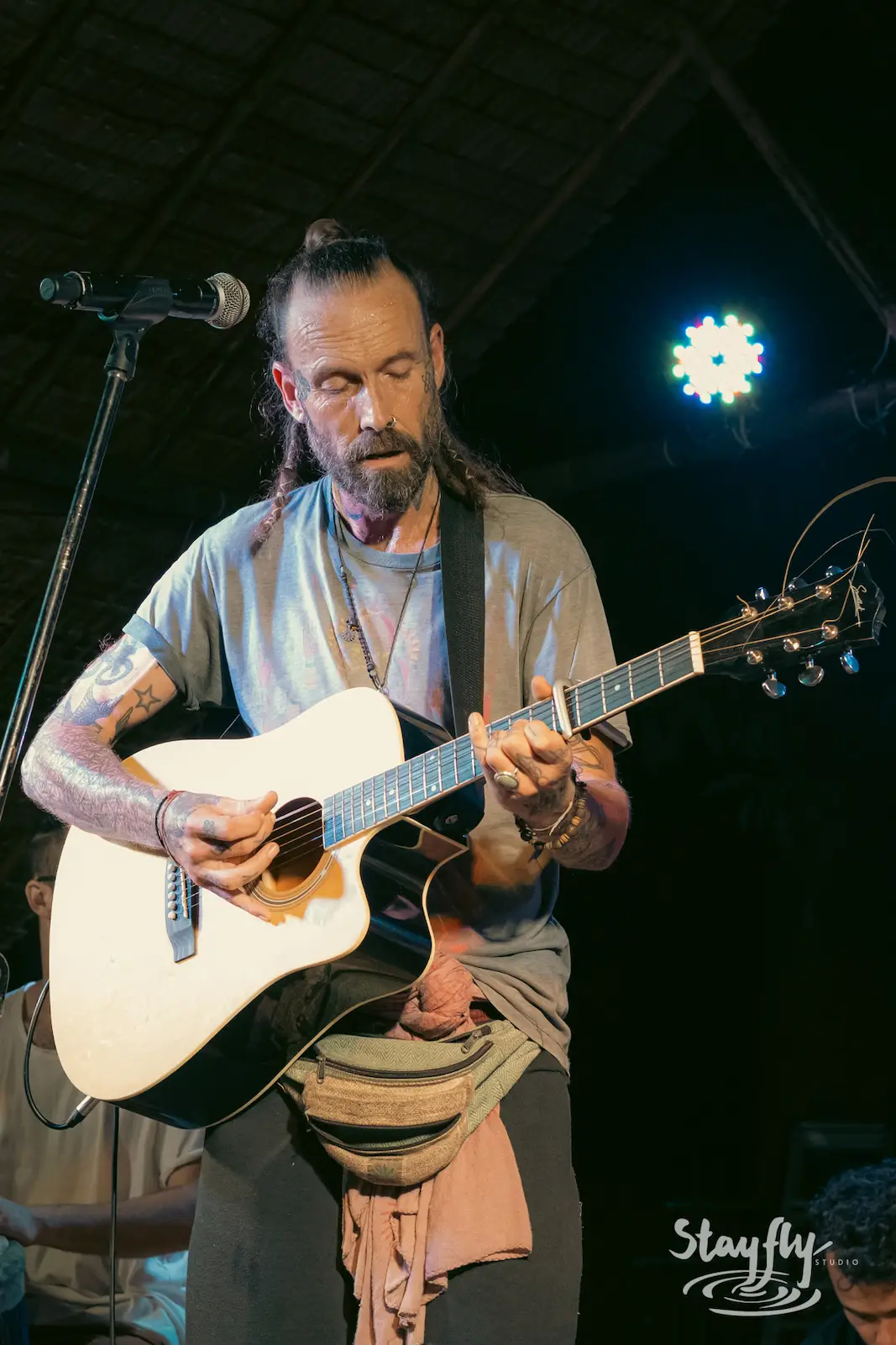 Man plays acoustic guitar under string lights.