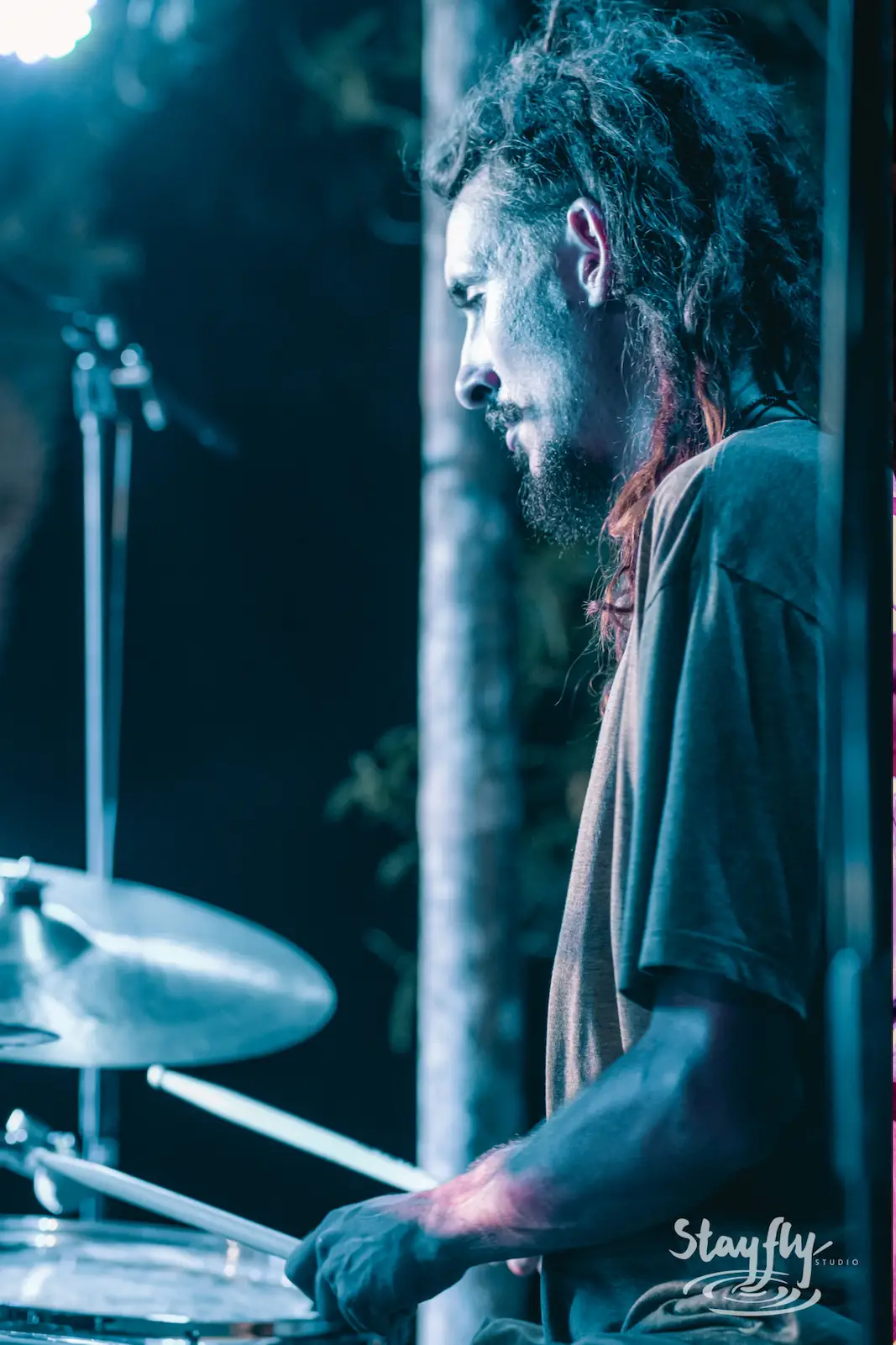 Drummer with dreadlocks playing cymbals at night.
