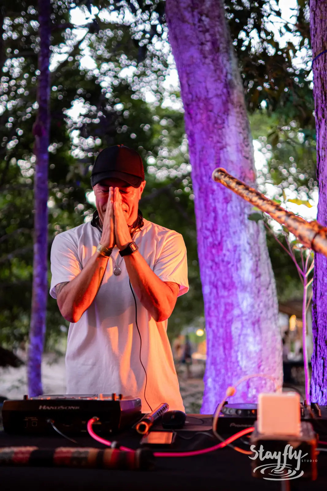 DJ with hands clasped near mixing gear.