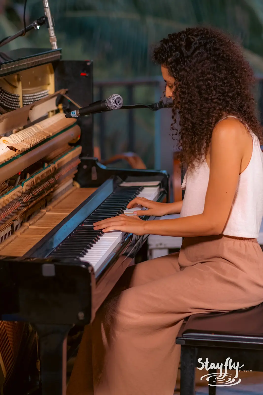 Woman playing upright piano on outdoor stage.