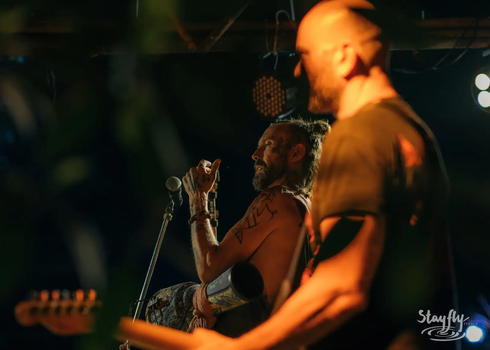 Two musicians close up, one speaking at mic.