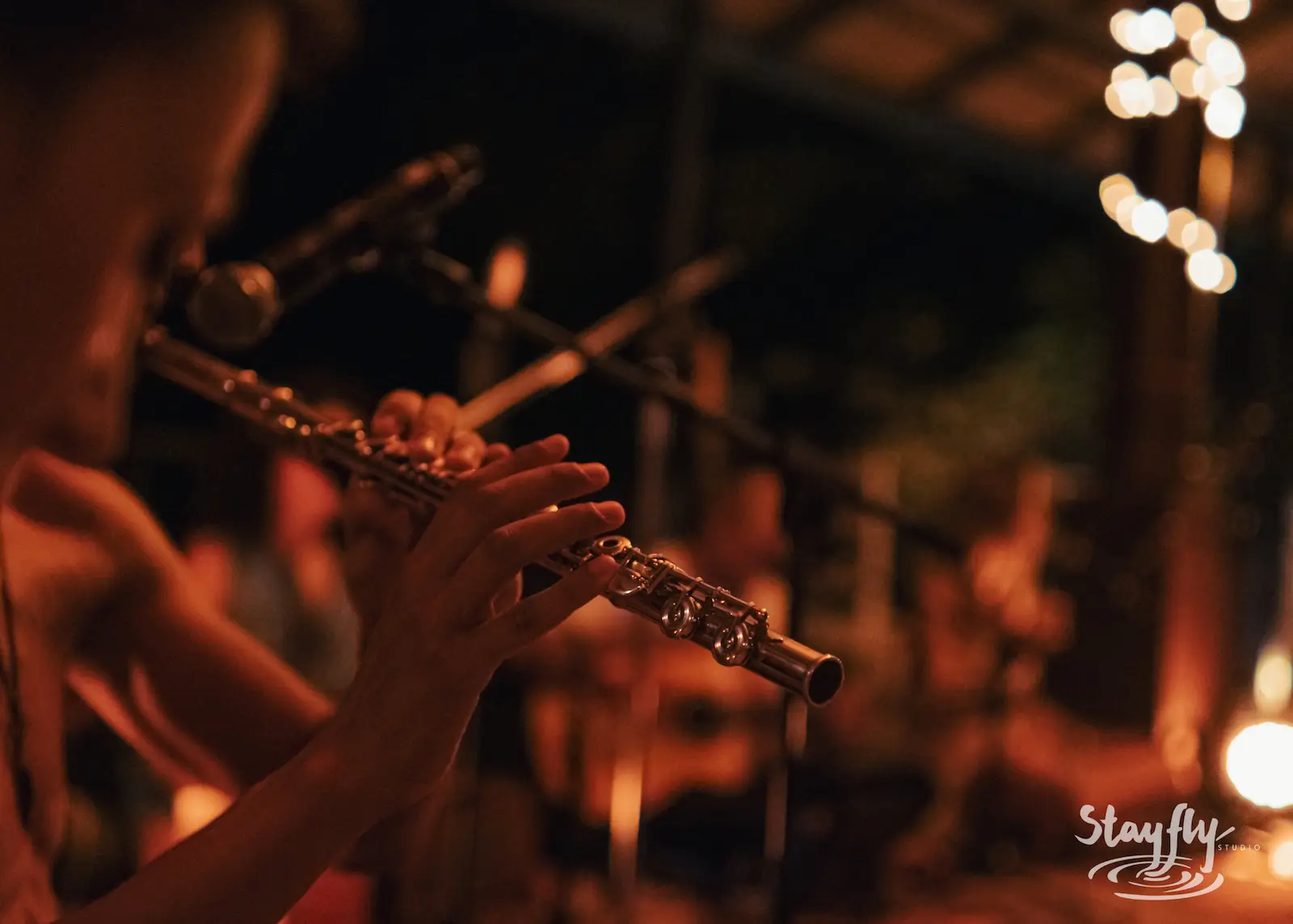 Flutist plays close-up under string lights.
