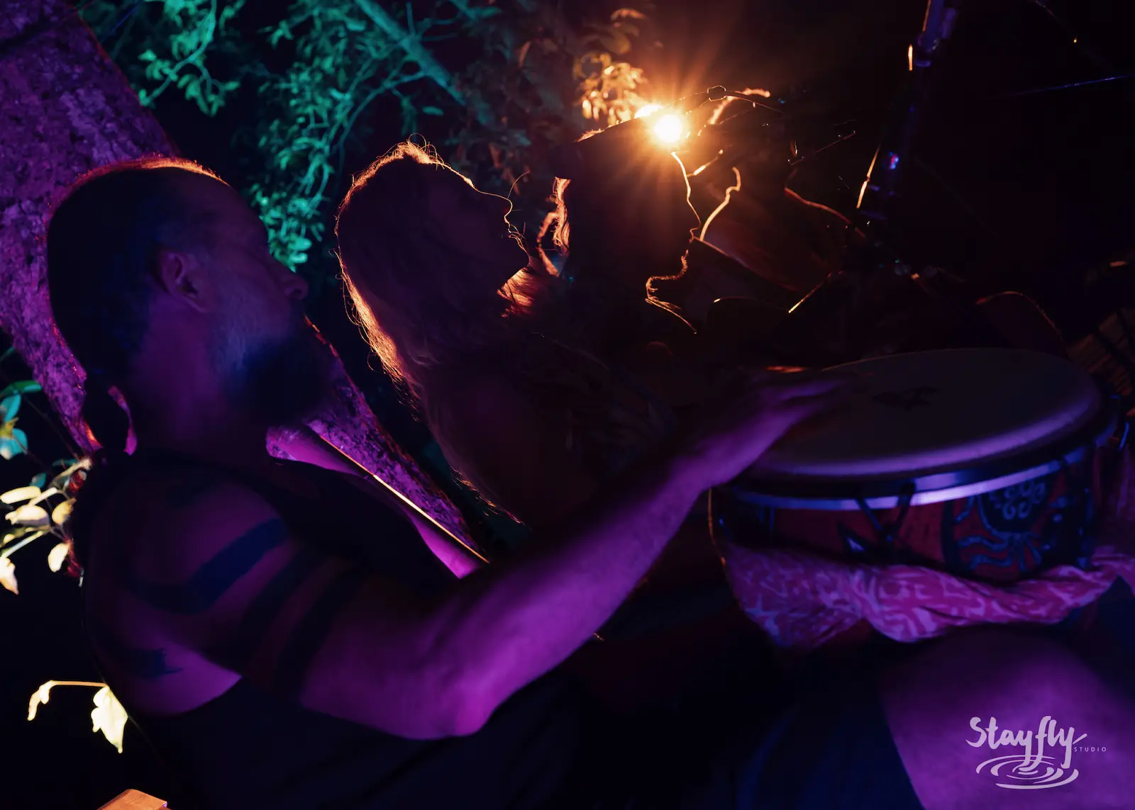 Drummer plays djembe amid purple night lighting.
