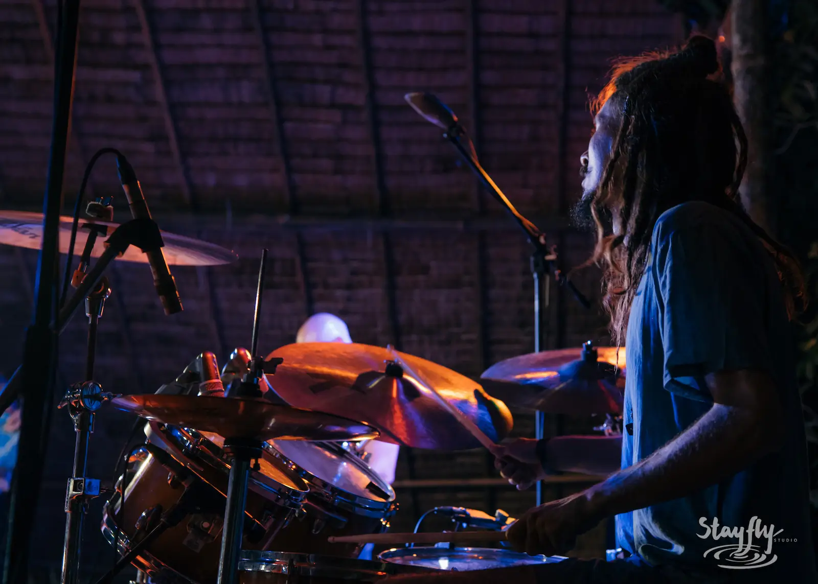 Drummer performs under purple stage lighting.