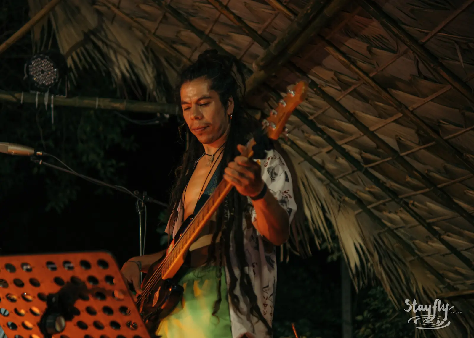 Guitarist performs under thatched roof at night.
