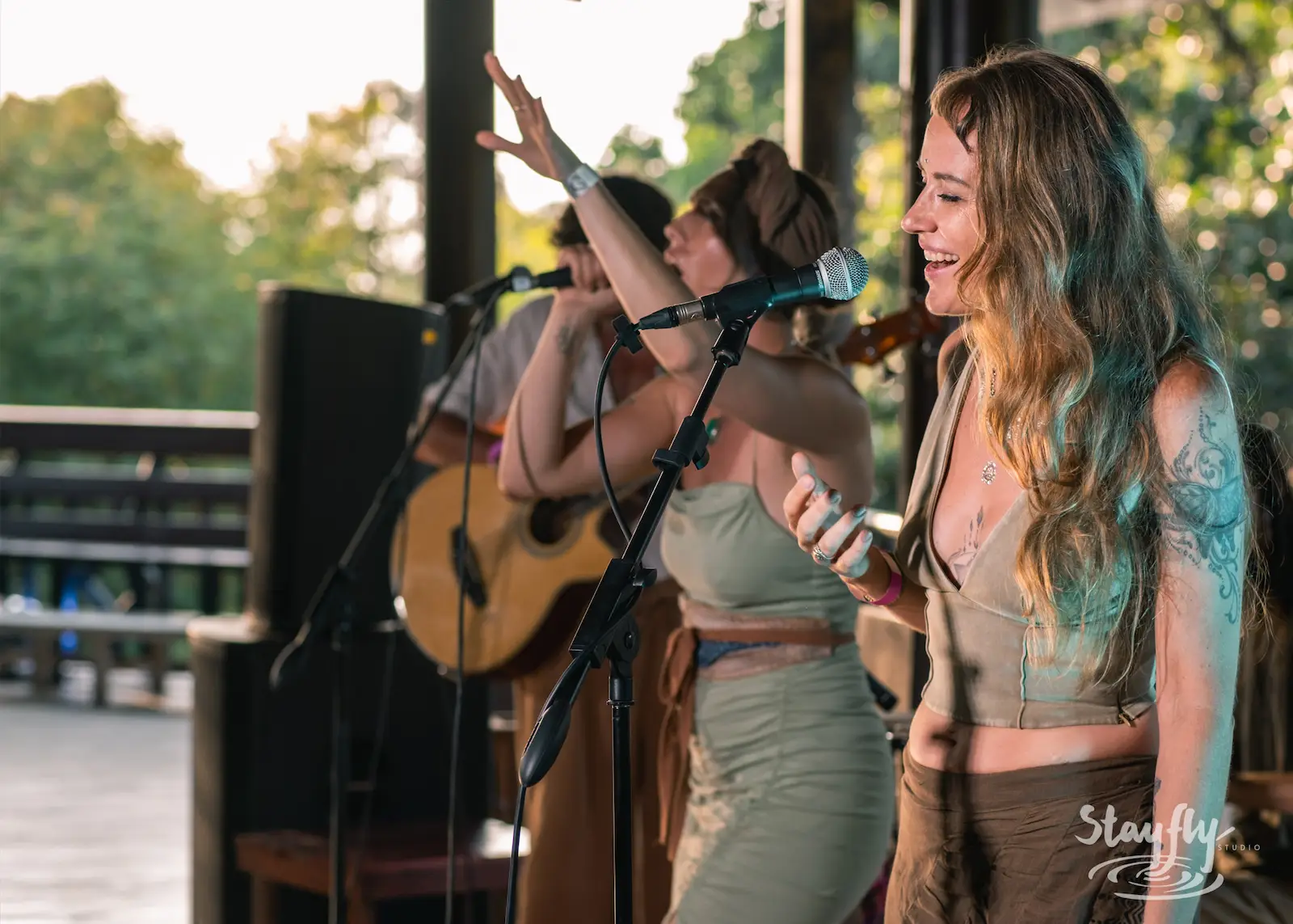 Three women sing on forest stage.