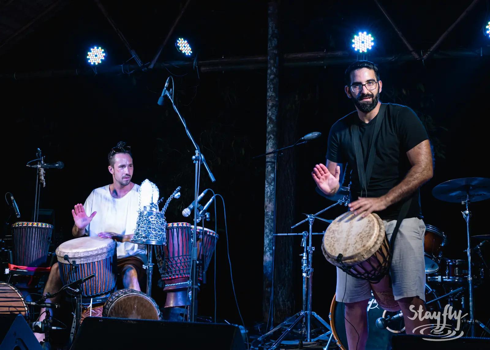Two men playing djembe drums on stage.