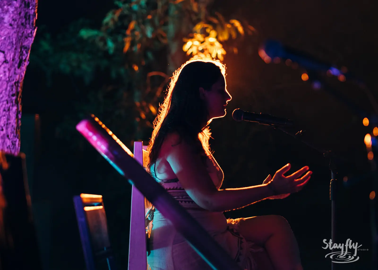 Woman singing at mic, backlit at night.