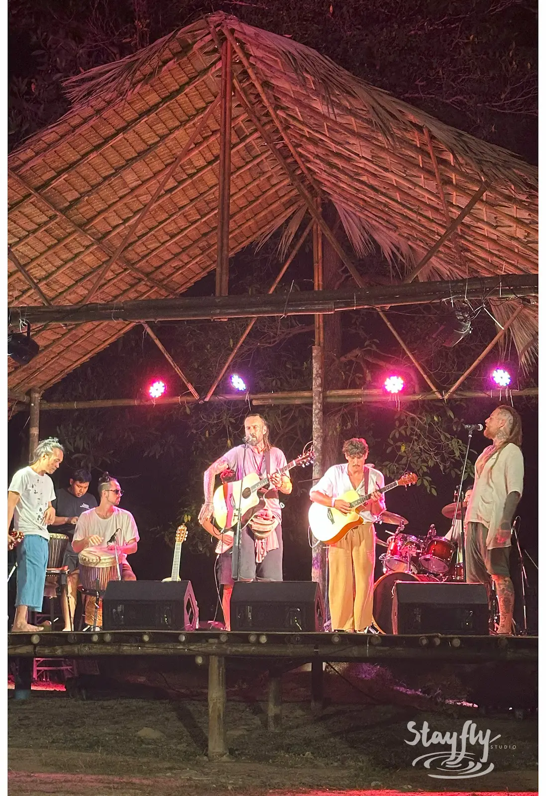 Band performing under thatched-roof stage.