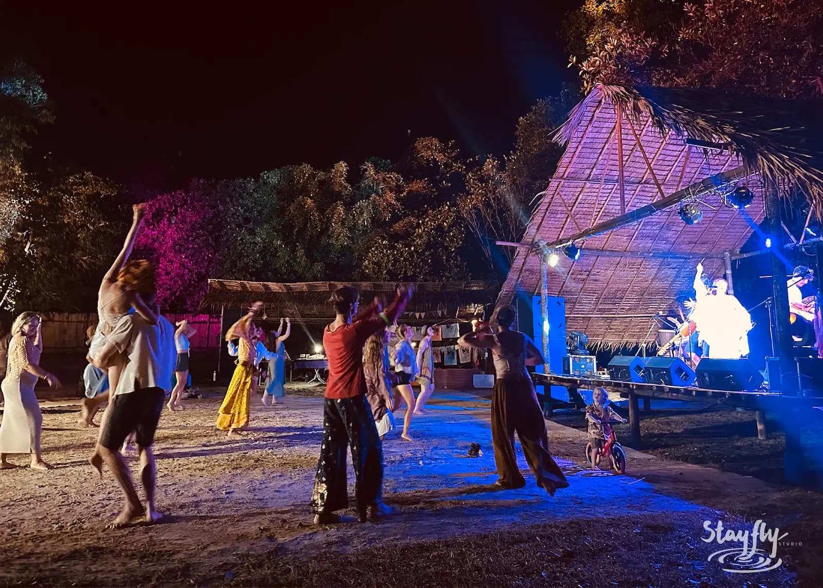 Night crowd dances before lit bamboo pyramid stage.