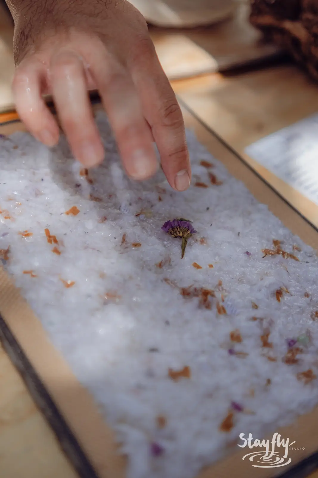Hand sprinkles flower petals onto bath salts.