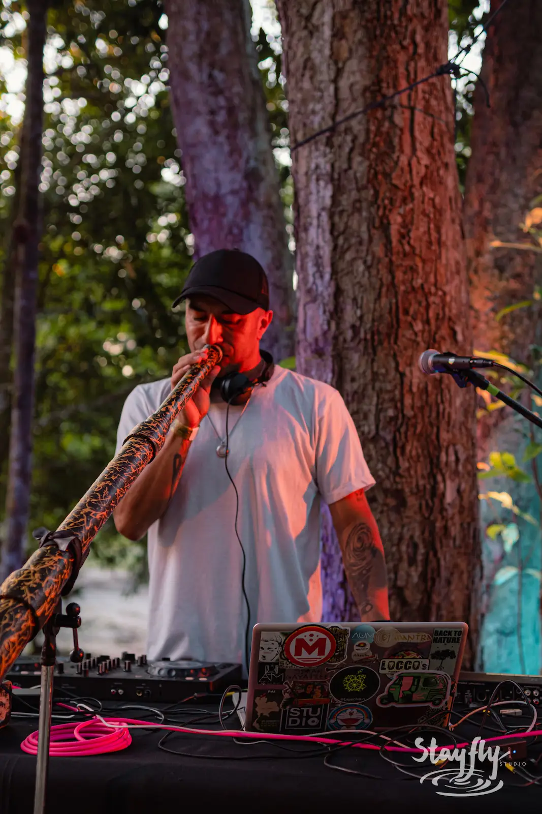 Man plays didgeridoo among forest trees.