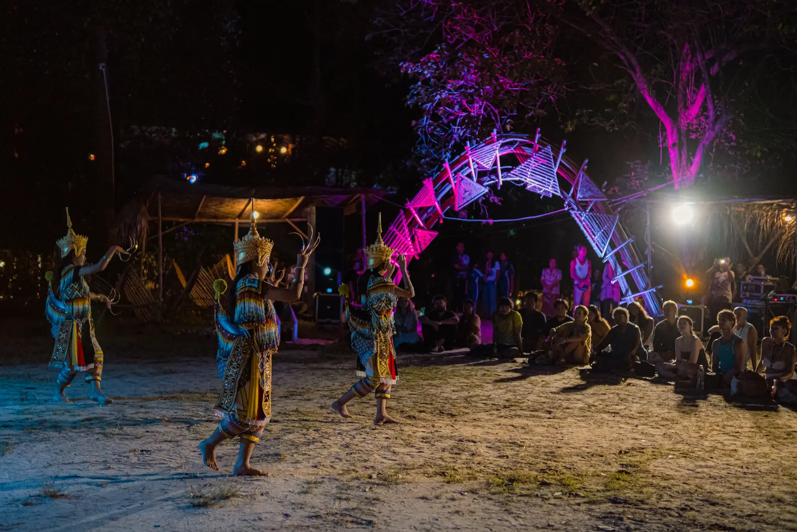 Dancers perform near glowing arch, crowd watches at night.