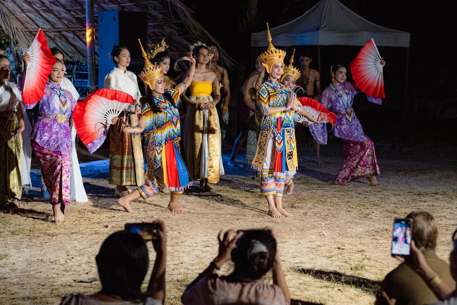 Women dancers with red fans perform for crowd.