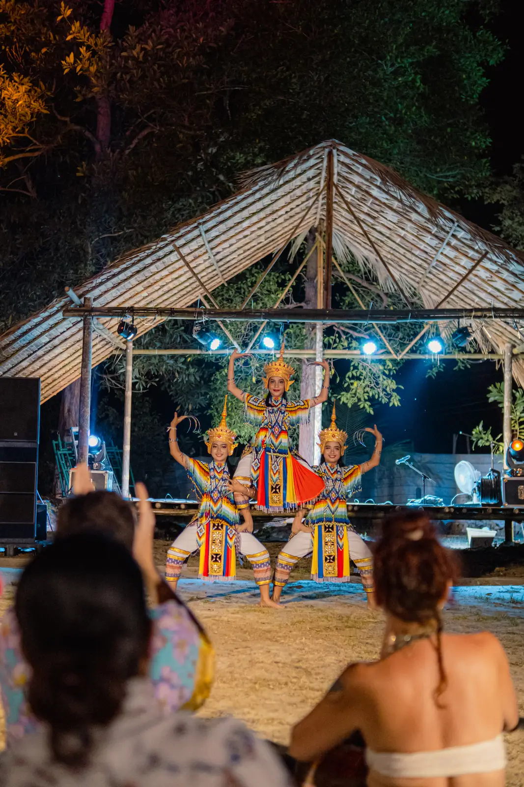 Three crowned dancers perform under thatched pavilion roof.
