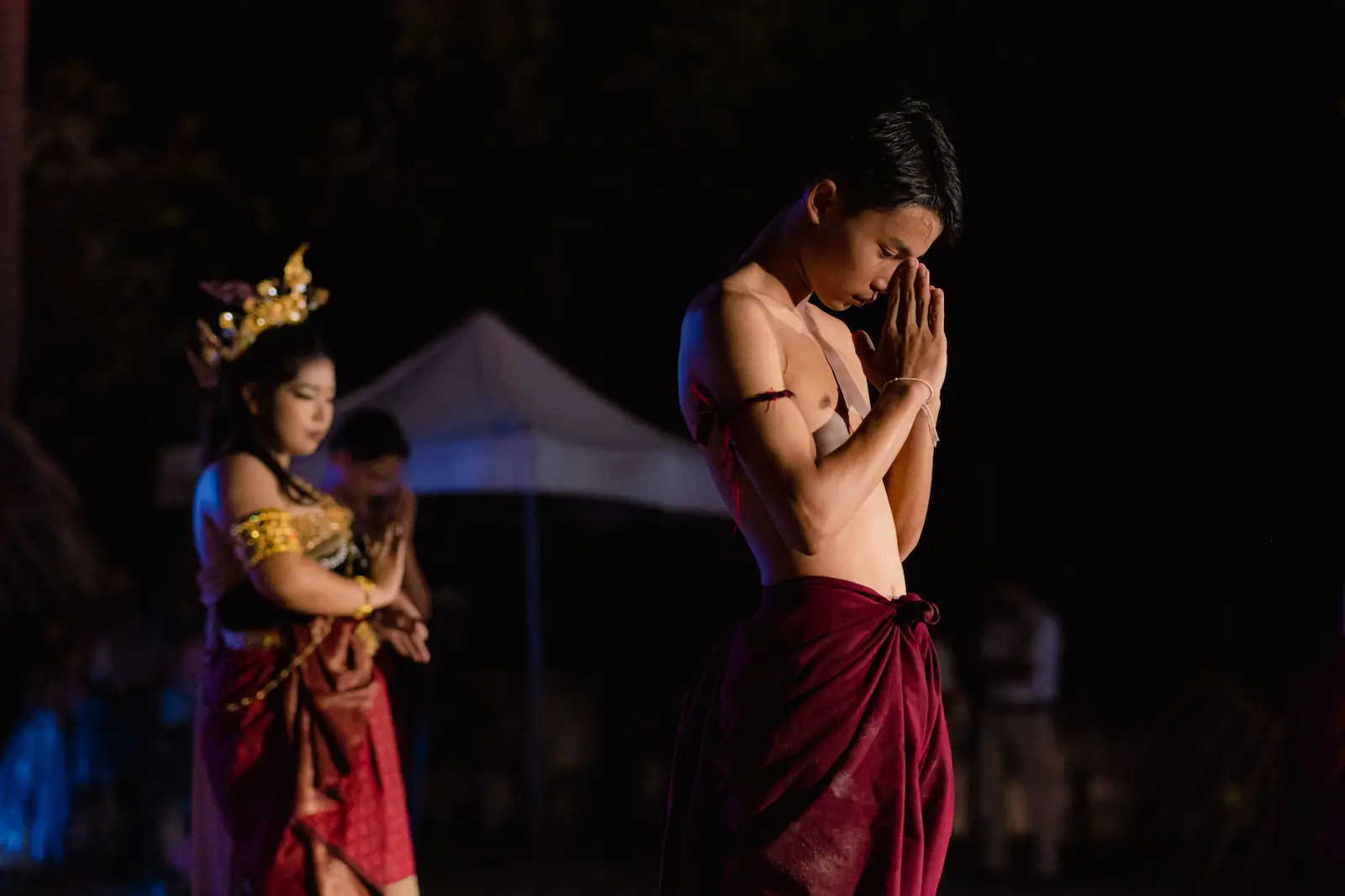 Young performer in red sarong bows in prayer.