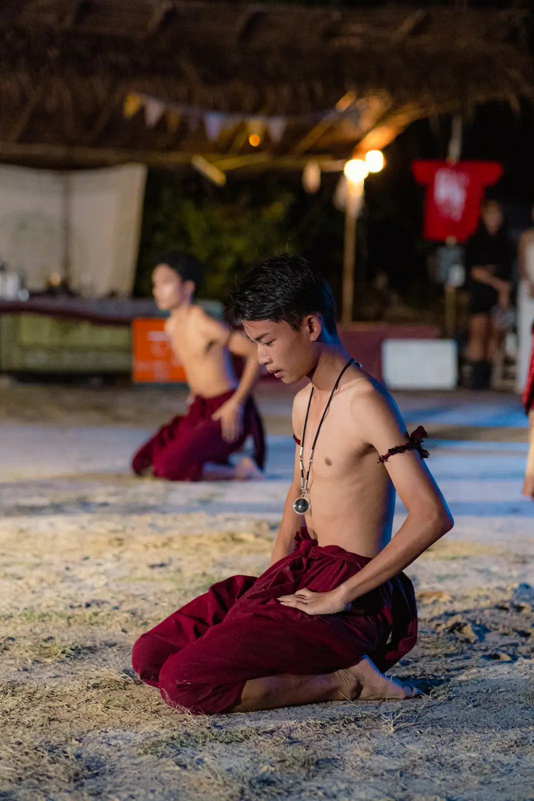 Young performer kneels in red sarong, eyes closed.