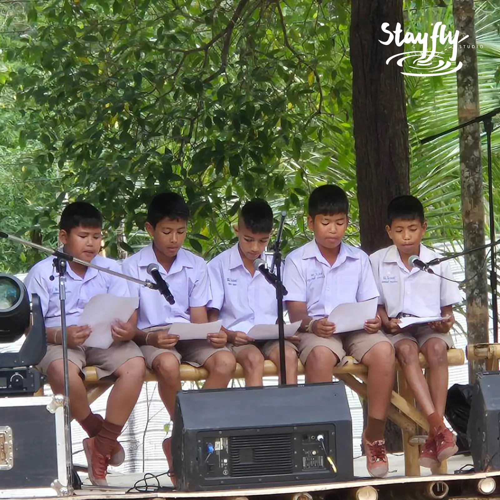 Five boys recite from scripts at outdoor microphones.