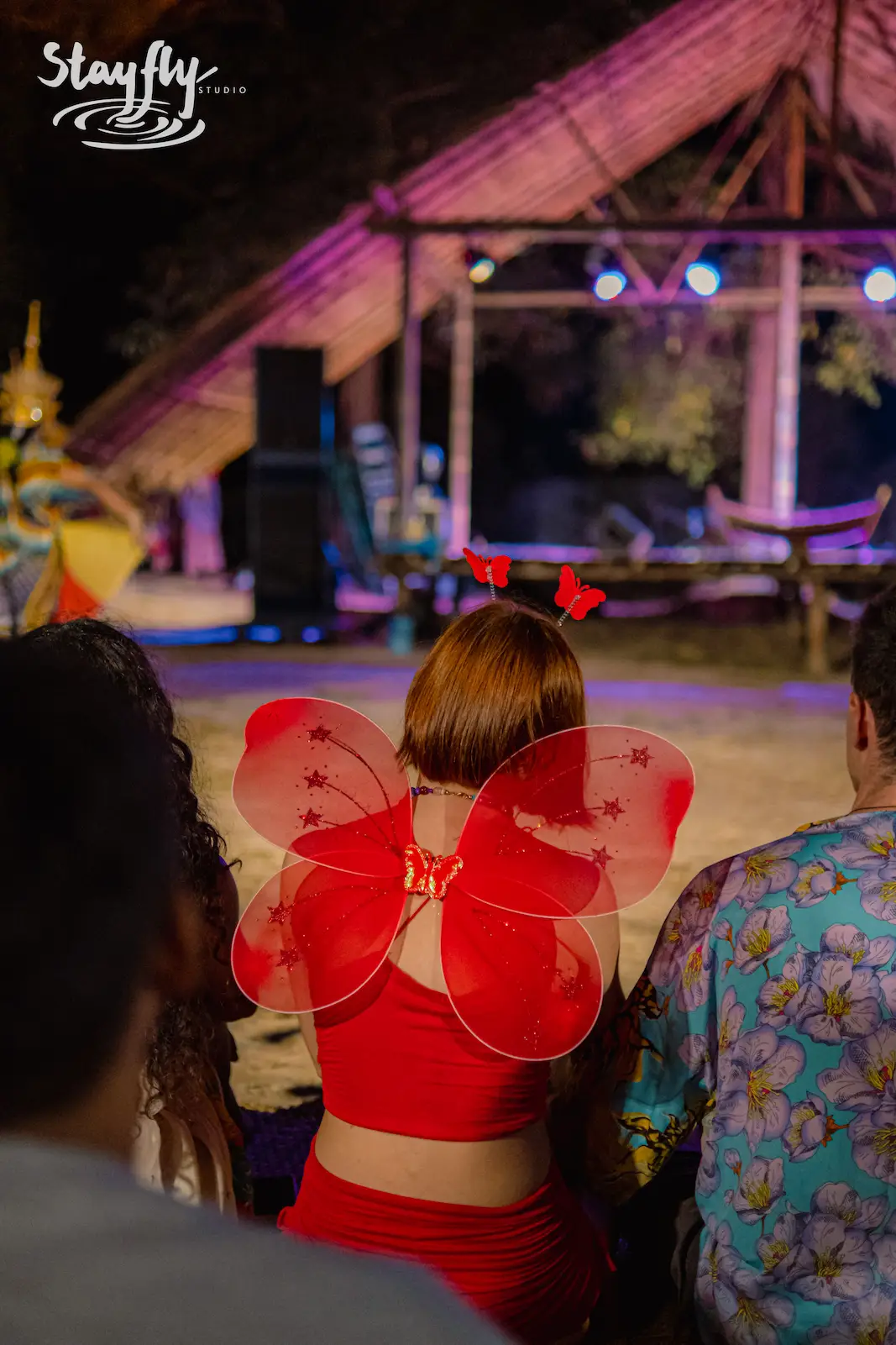 Guest in red butterfly wings amid night crowd.