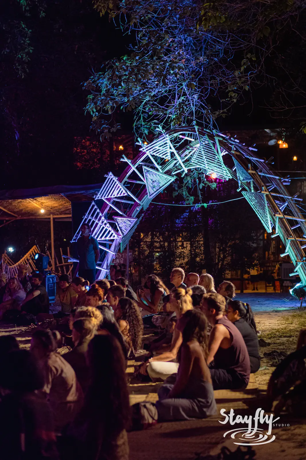 Crowd gathered beneath glowing lit archway at night.