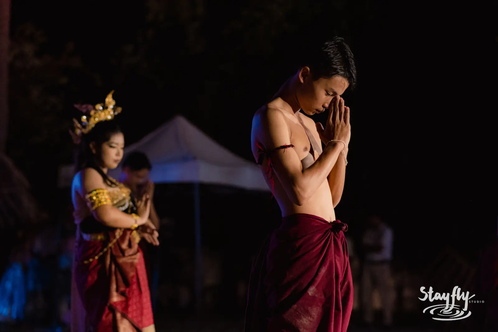 Performer in maroon wrap, hands in prayer.