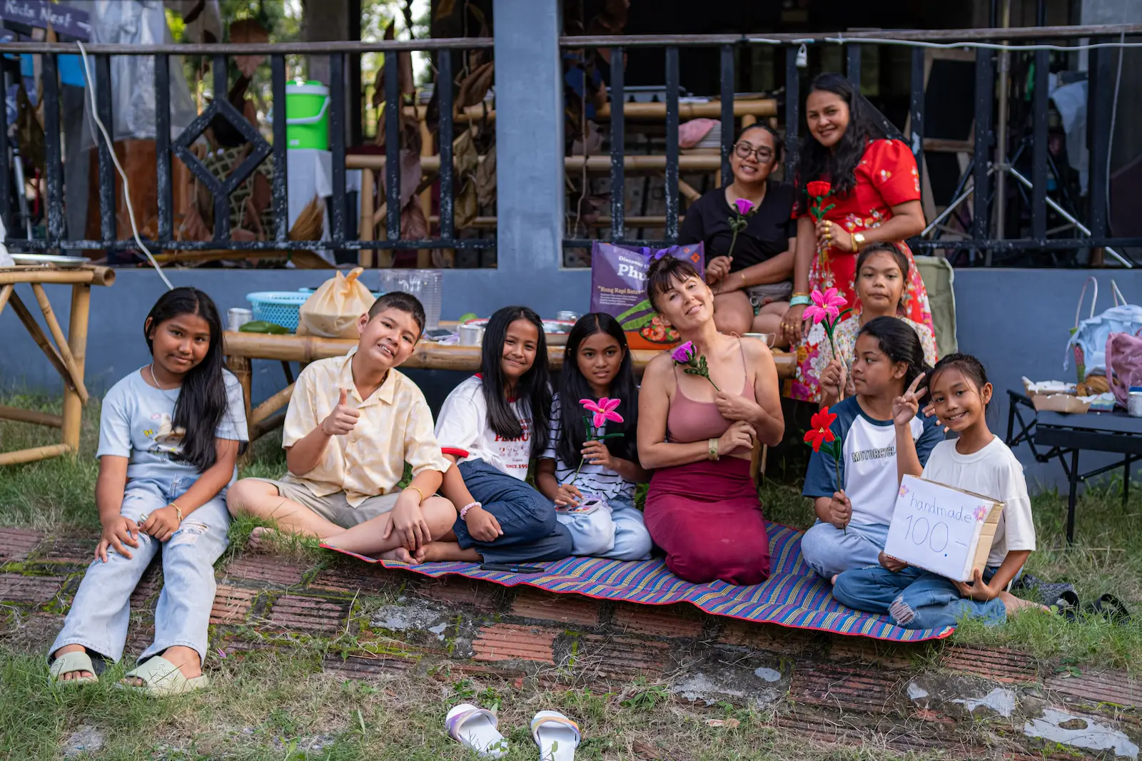 Group of children and adults pose on mat outdoors.