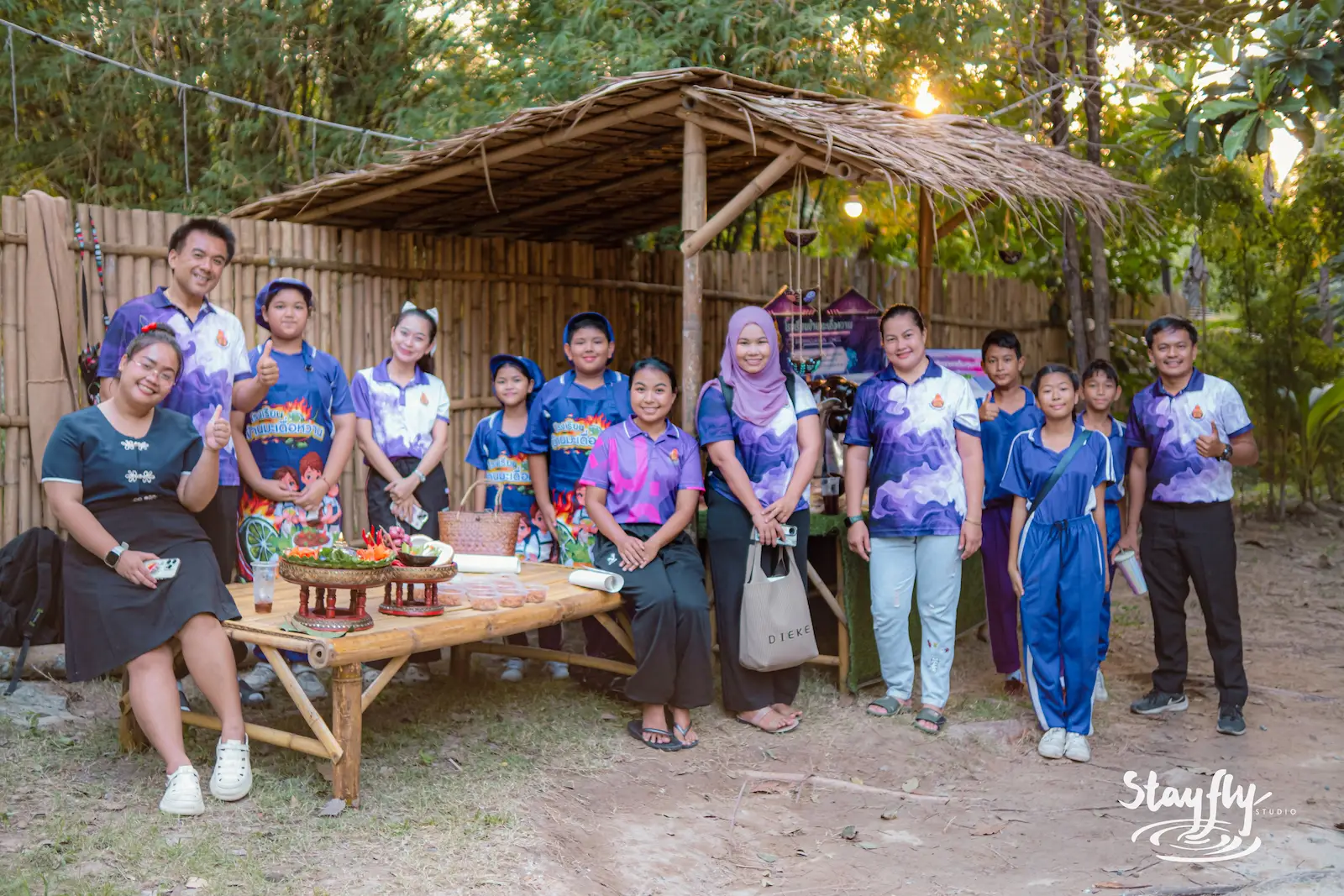School group poses together under thatched shelter.