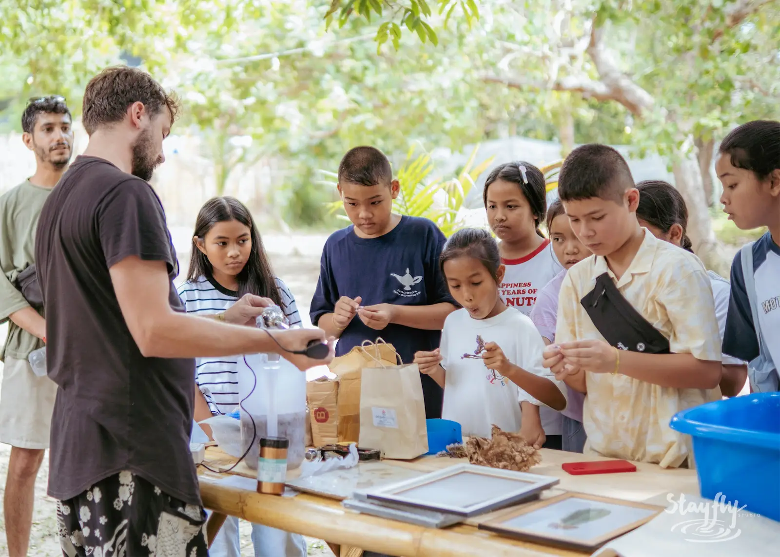 Man teaches children at outdoor workshop table.