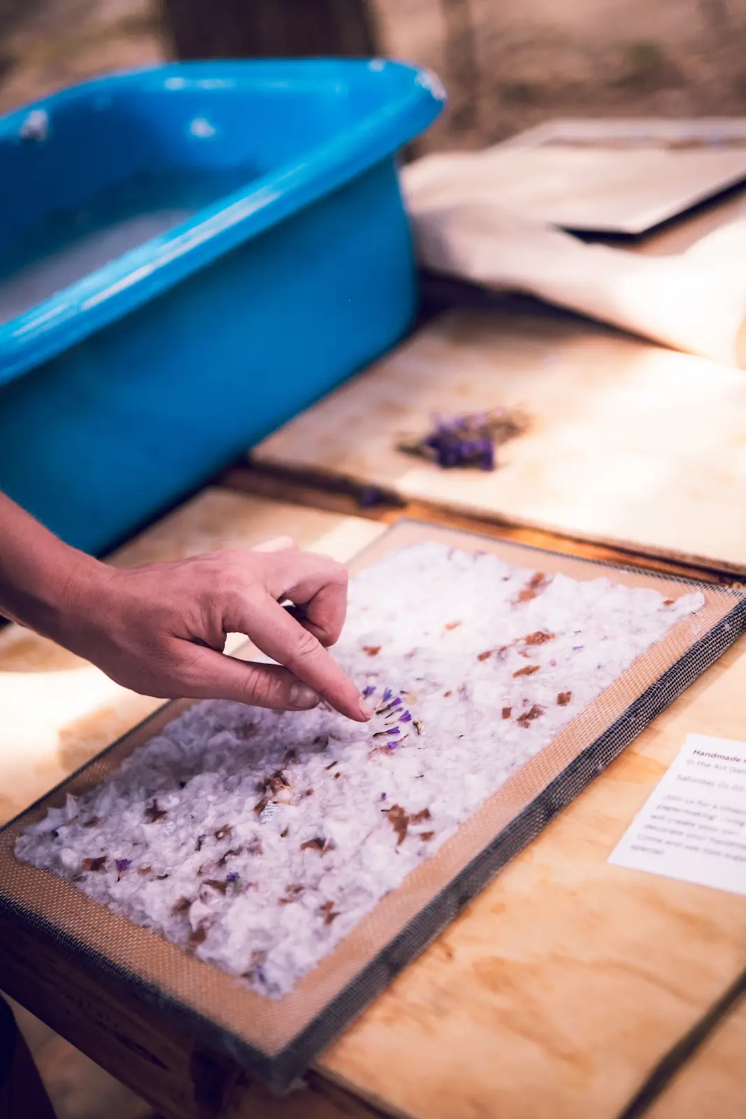 Hand arranges petals on wet handmade paper.