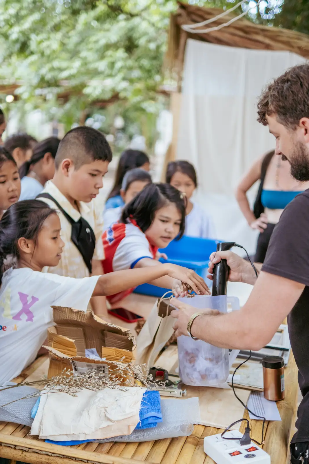 Children watch adult demonstrate papermaking blender device.