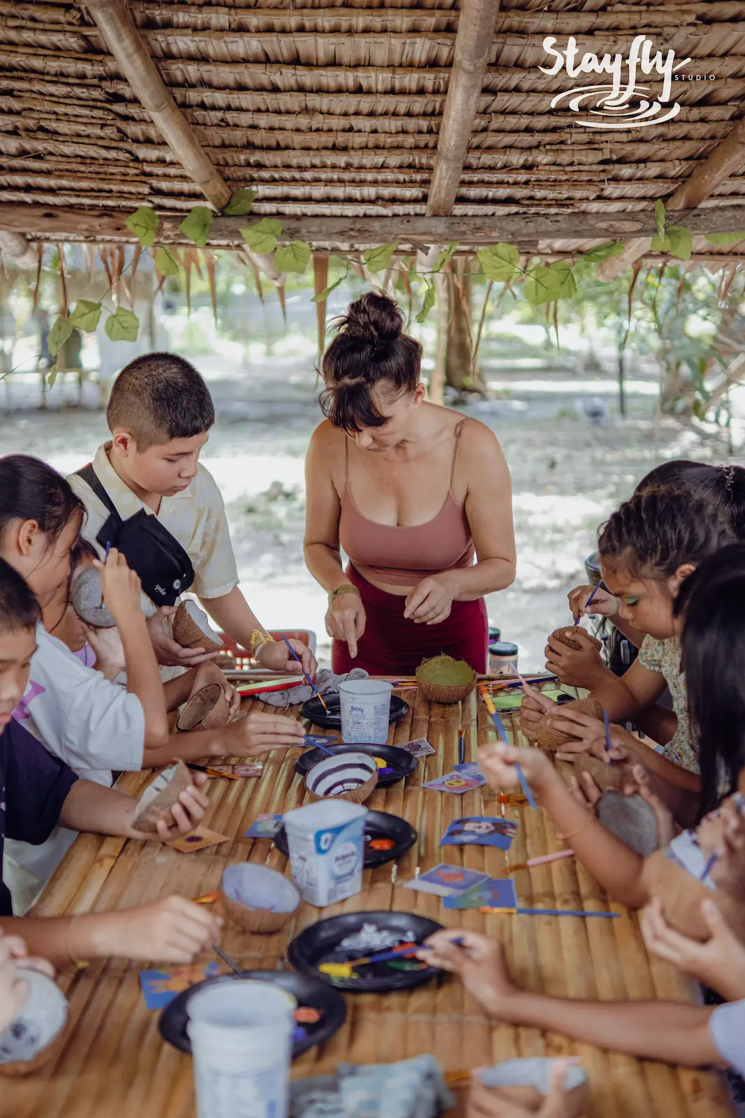 Children and adult painting coconut shells at table.