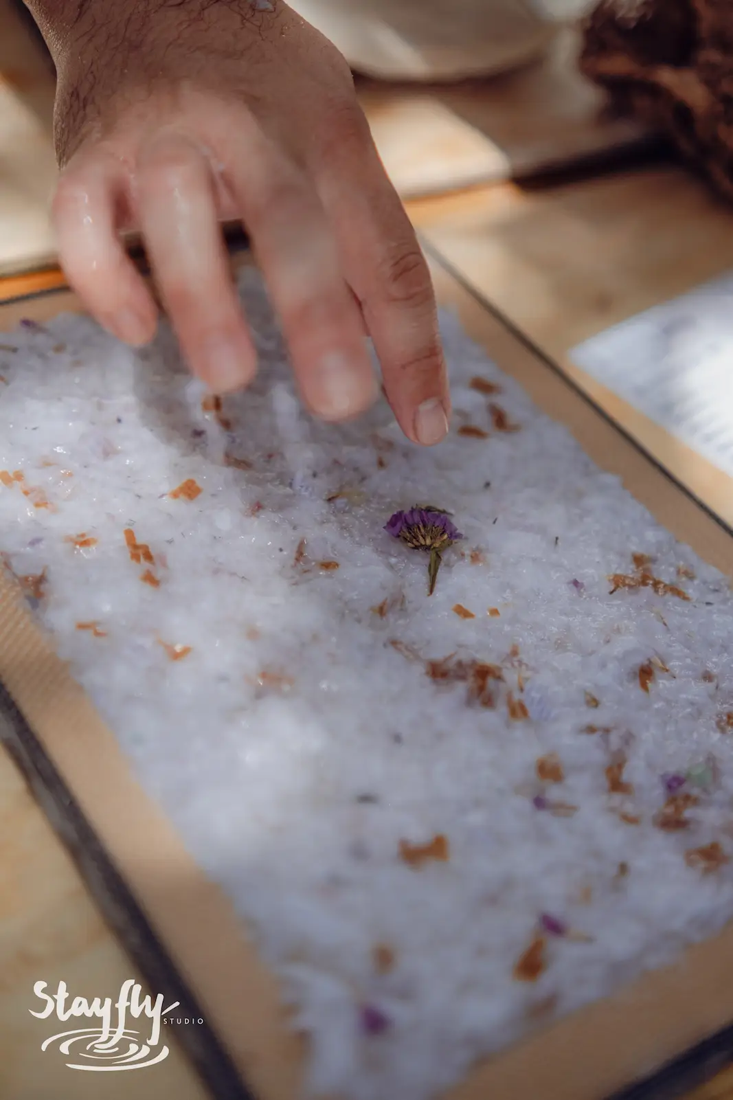 Hand placing single flower on paper pulp sheet.