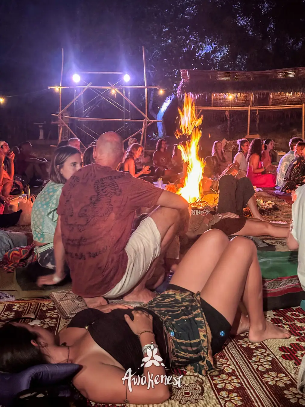 Crowd gathered around bonfire at night.