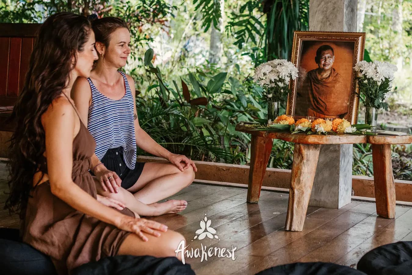 Two women meditate before monk memorial portrait.